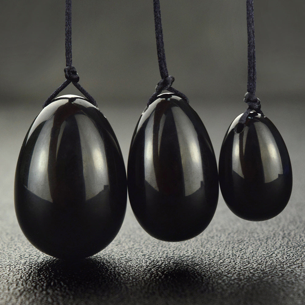 Obsidian Yoni-Eier mit Rückholbändchen auf dunklem Hintergrund