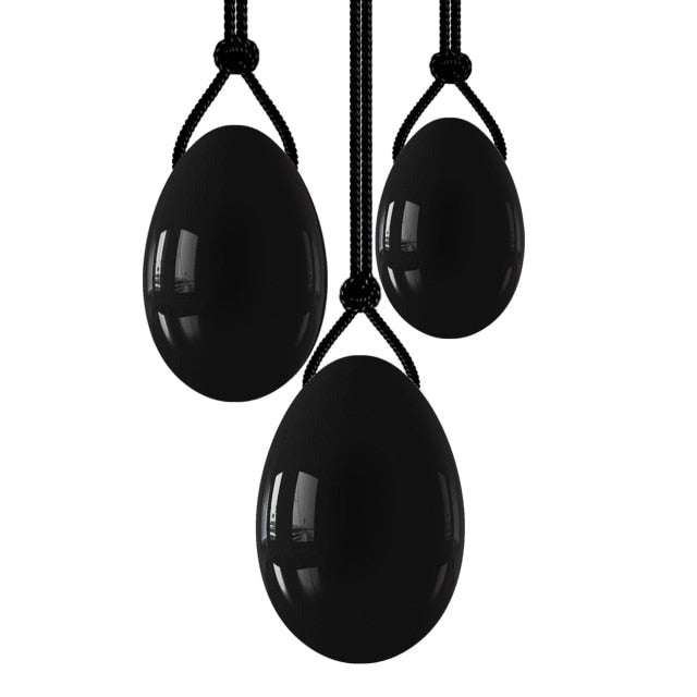 Drei schwarze Obsidian Yoni-Eier mit Rückholbändchen auf weißem Hintergrund